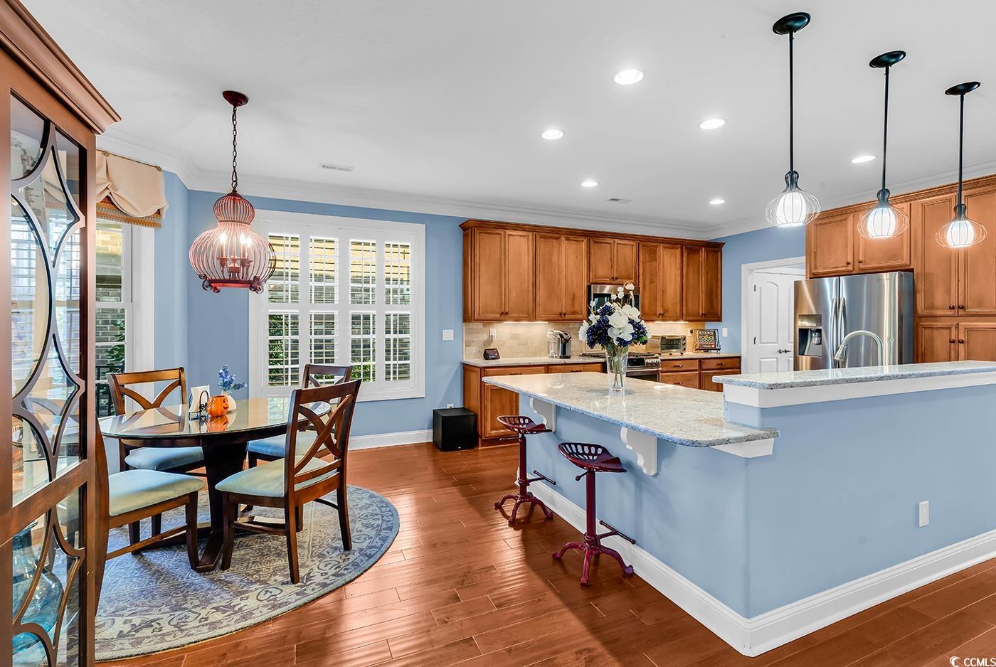 956 Corrado Street Myrtle Beach, SC 29572 - Photo 6 of 38 Kitchen with brown cabinetry, decorative light fixtures, a kitchen island with sink, ornamental molding, and light stone counters