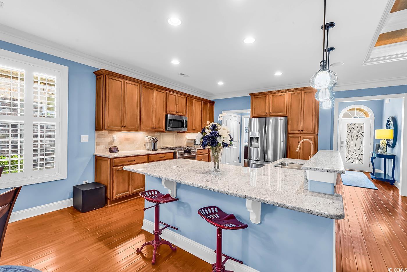 956 Corrado Street Myrtle Beach, SC 29572 - Photo 7 of 38 Kitchen featuring brown cabinets, a breakfast bar area, light stone counters, ornamental molding, and decorative backsplash