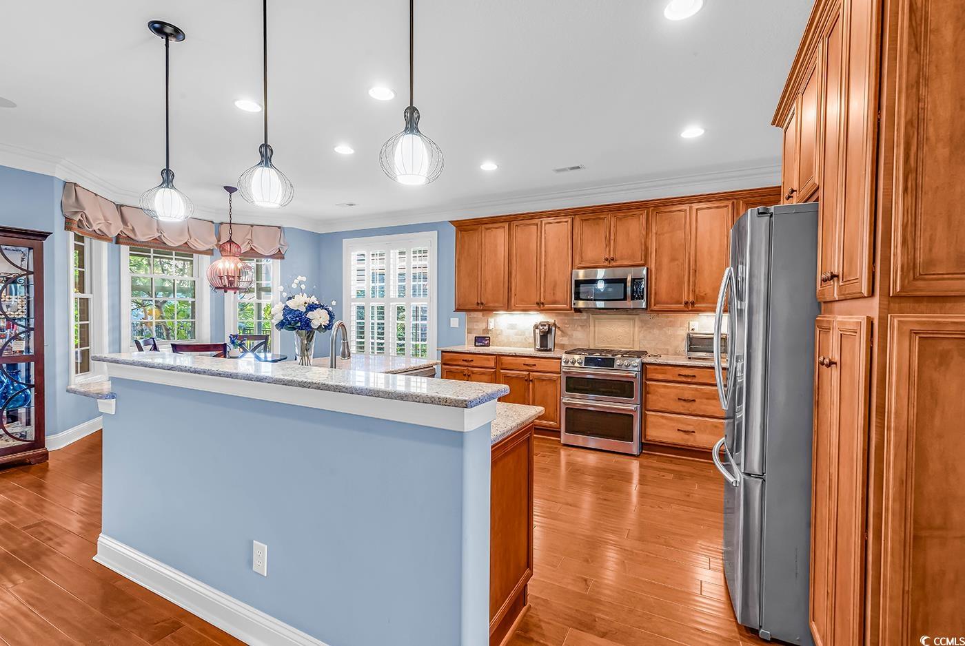 956 Corrado Street Myrtle Beach, SC 29572 - Photo 8 of 38 Kitchen featuring brown cabinets, crown molding, hanging light fixtures, backsplash, and appliances with stainless steel finishes
