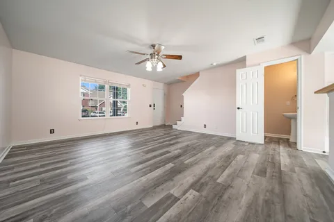 an empty room with wooden floor chandelier fan and windows