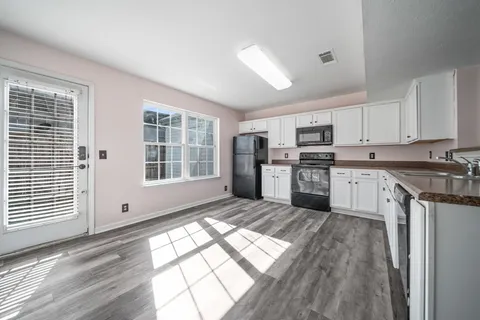 a kitchen with stainless steel appliances granite countertop a stove a sink dishwasher a refrigerator and white cabinets with wooden floor