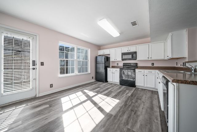 a kitchen with stainless steel appliances granite countertop a stove a sink dishwasher a refrigerator and white cabinets with wooden floor