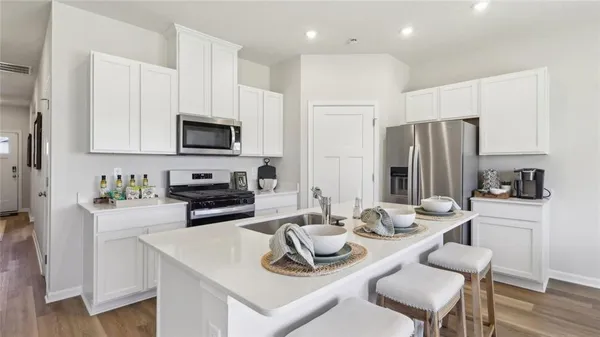 a kitchen with a refrigerator a stove a sink dishwasher a dining table and chairs with wooden floor