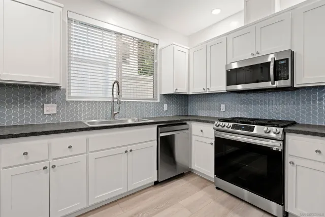 a kitchen with stainless steel appliances granite countertop grey cabinets a stove a sink and a microwave