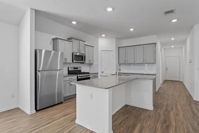 a kitchen with stainless steel appliances granite countertop a refrigerator a sink dishwasher a stove and a microwave oven on wooden floor