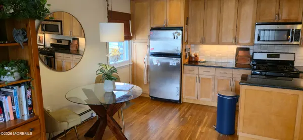 a kitchen with stainless steel appliances granite countertop a refrigerator a stove a sink a dining table and chairs with wooden floor