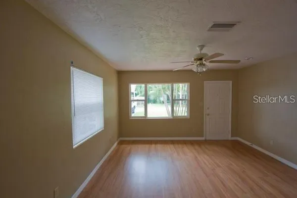 an empty room with wooden floor fan and windows