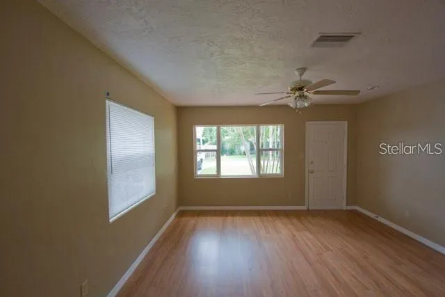an empty room with wooden floor fan and windows