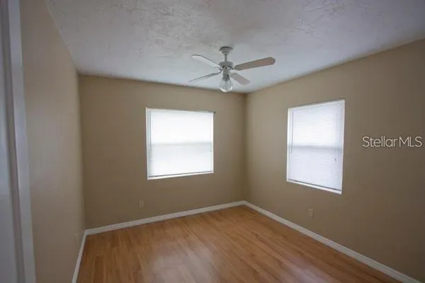 an empty room with wooden floor ceiling fan and windows