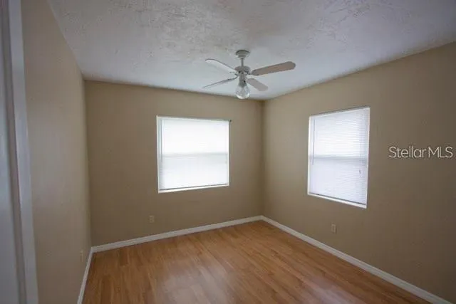 an empty room with wooden floor ceiling fan and windows