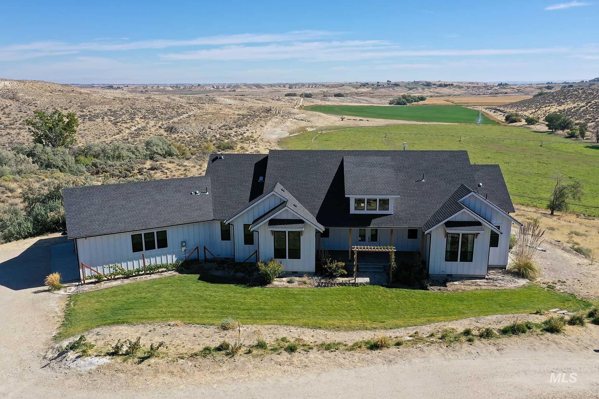 876 Coyote Gulch Road Adrian, OR 97901 - Photo 1 of 50 White exterior siding, dark roof, expansive front lawn, multiple windows, and a pergola over the entry