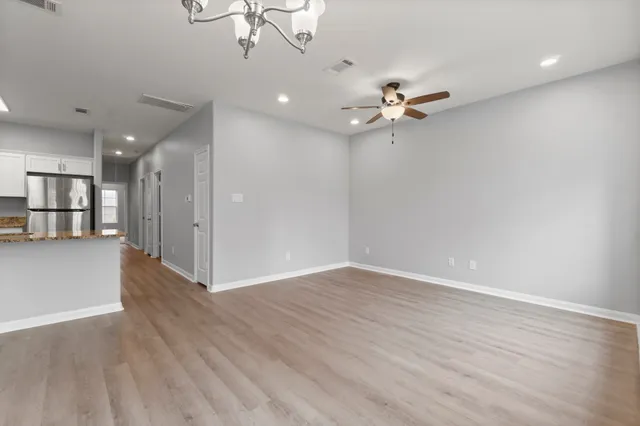 an empty room with wooden floor ceiling fan and refrigerator
