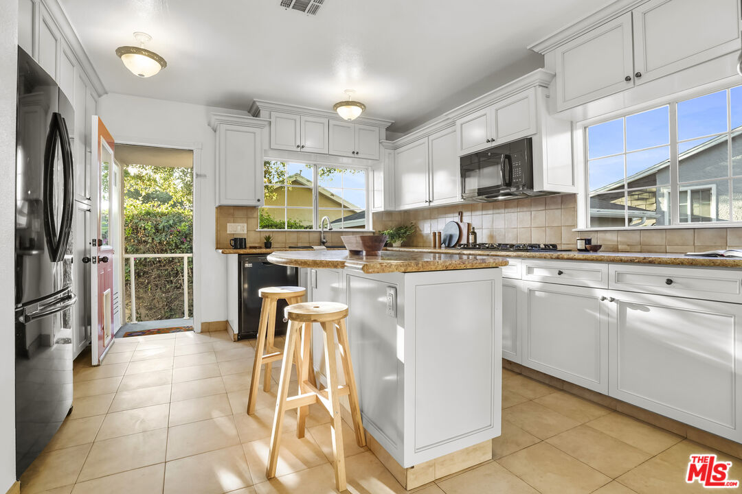 10129 Plainview Avenue Tujunga, CA 91042 - Photo 15 of 51 a kitchen with stainless steel appliances kitchen island granite countertop a refrigerator oven a sink dishwasher and white cabinets next to a window