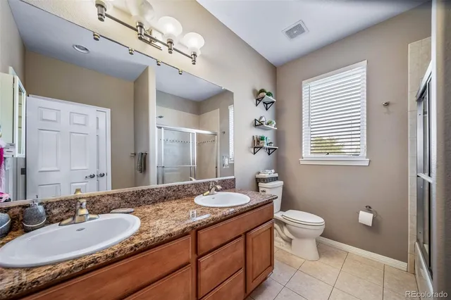 a bathroom with a granite countertop double vanity sink a mirror and a toilet