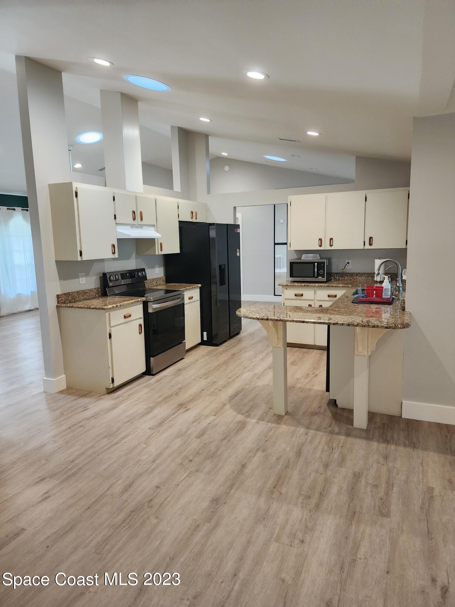 708 Fishtail Palm Boulevard Melbourne, FL 32901 - Photo 8 of 33 a kitchen with stainless steel appliances kitchen island granite countertop a stove a sink a refrigerator and white cabinets with wooden floor