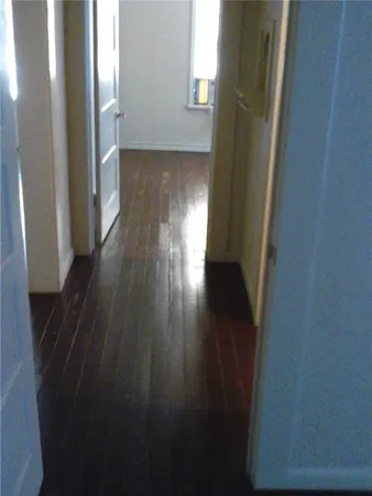 a view of a hallway to an empty room with wooden floor and a window