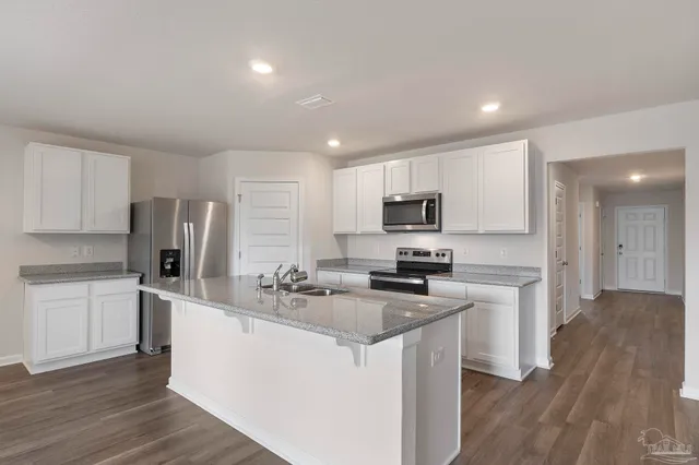 a kitchen with stainless steel appliances granite countertop a stove top oven a sink a refrigerator and white cabinets