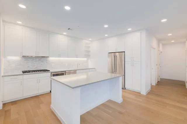 a kitchen with stainless steel appliances granite countertop a sink a stove a refrigerator and white cabinets with wooden floor