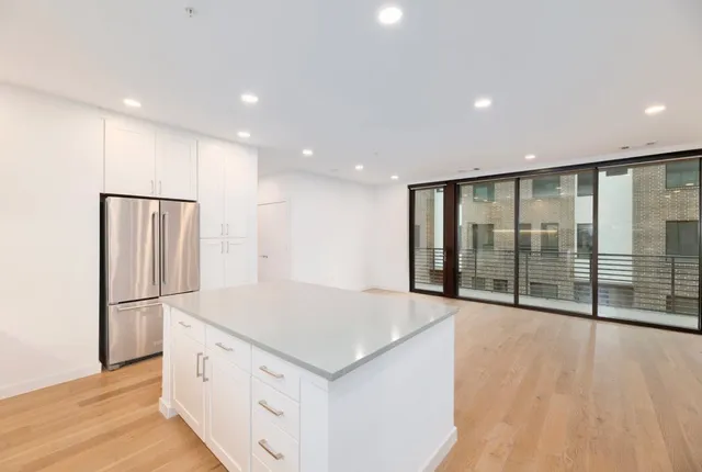a view of an empty room with wooden floor and a kitchen