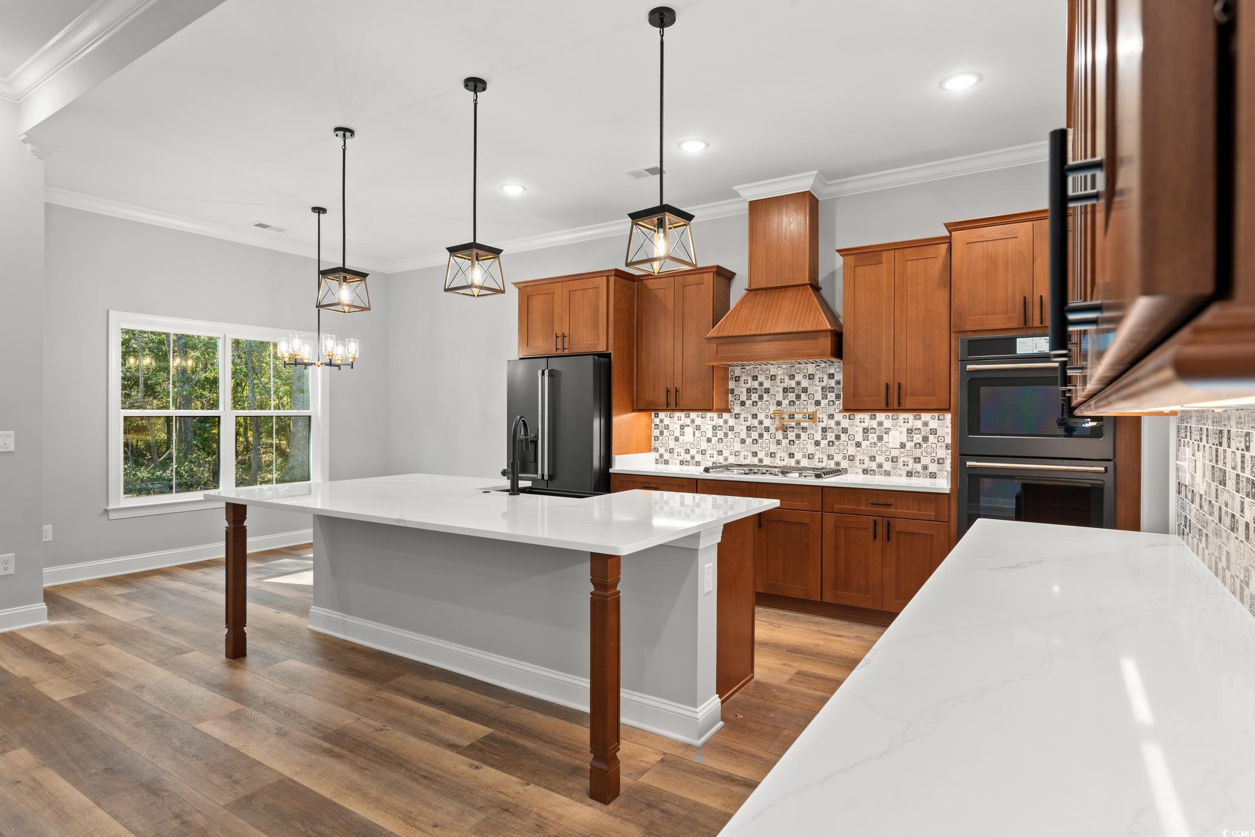 8016 Old Reaves Ferry Road Conway, SC 29526 - Photo 5 of 33 Kitchen featuring brown cabinets, backsplash, a kitchen island with sink, crown molding, and hanging light fixtures