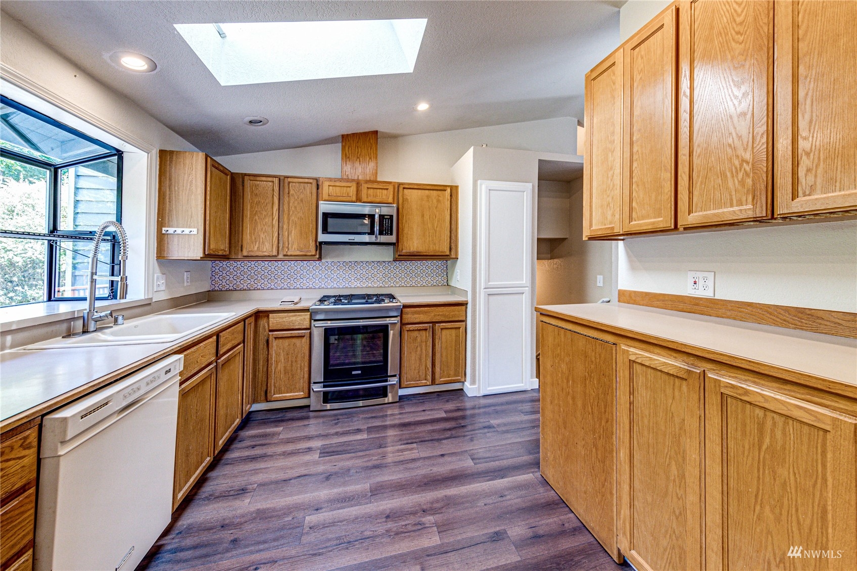 1027 233rd Place Southwest Bothell, WA 98021 - Photo 6 of 27 a kitchen with stainless steel appliances a stove top oven a sink dishwasher a refrigerator and a dining table with wooden floor