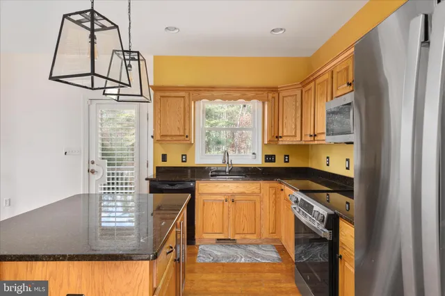 a kitchen with stainless steel appliances granite countertop a refrigerator a sink dishwasher a stove and a dining table with wooden floor