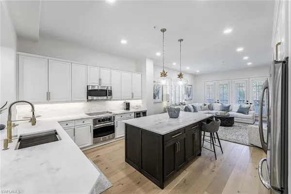 a large white kitchen with stainless steel appliances a stove a sink a oven a dining table and chairs