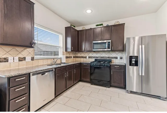 a kitchen with granite countertop a refrigerator stove top oven and sink