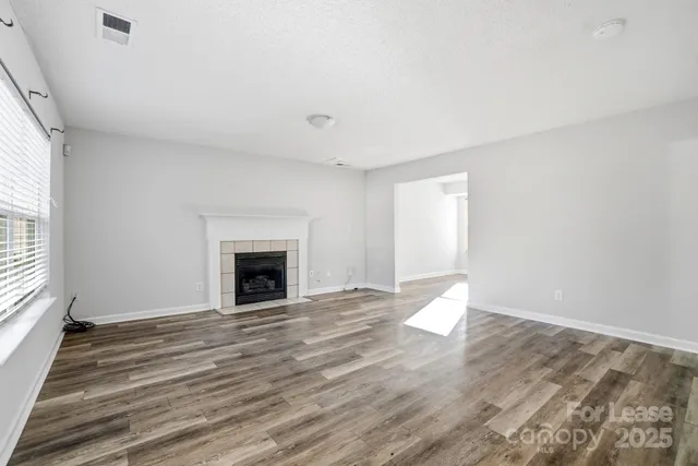 an empty room with wooden floor fireplace and windows