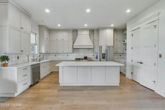 a large white kitchen with kitchen island a sink stainless steel appliances and white cabinets