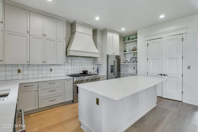 a large kitchen with stainless steel appliances granite countertop a stove a sink a refrigerator and white cabinets with wooden floor