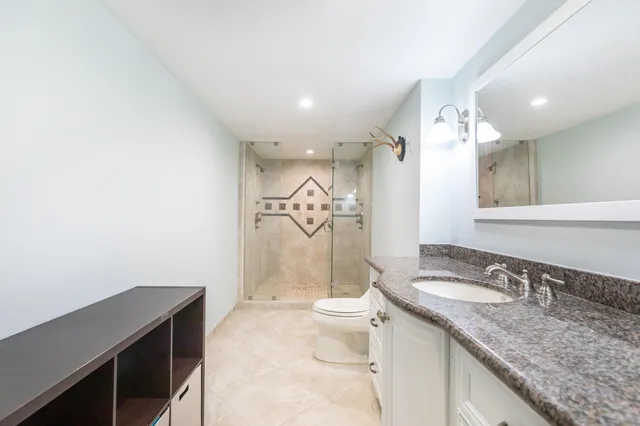 a spacious bathroom with a granite countertop sink a toilet a mirror and shower