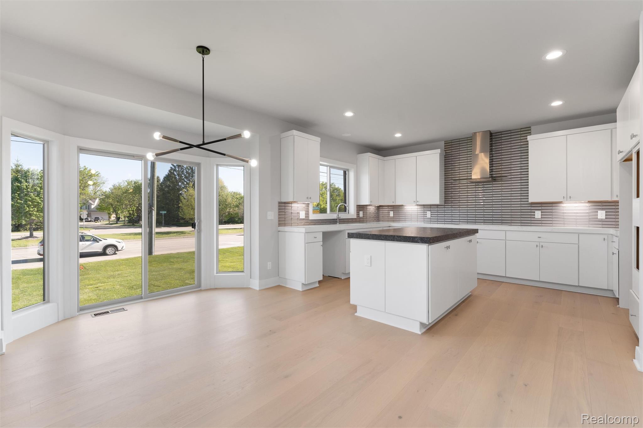 3989 Capstan Court Troy, MI 48083 - Photo 6 of 19 Kitchen with dark countertops, white cabinetry, decorative backsplash, suspended lighting, and light wood-type flooring