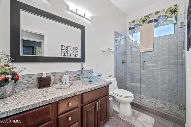a bathroom with a granite countertop sink a toilet a mirror and shower