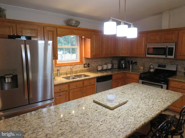 a kitchen with stainless steel appliances granite countertop a stove a sink a refrigerator and a wooden cabinets