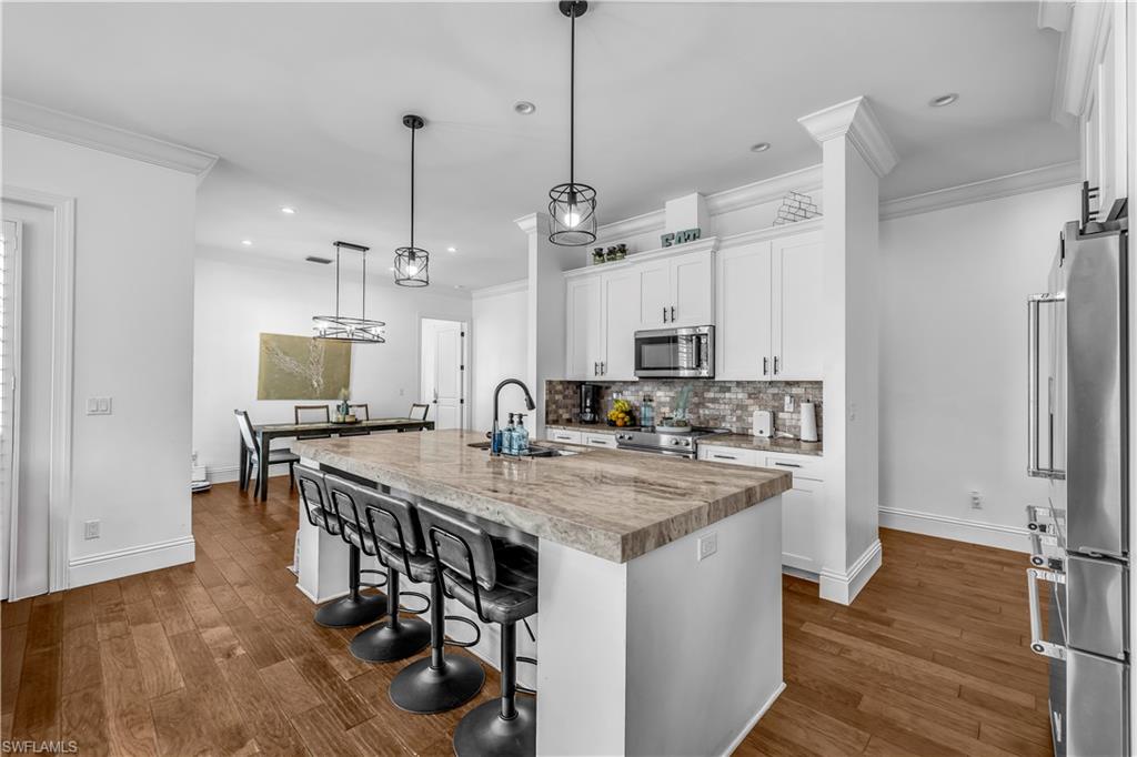 11141 Palmetto Ridge Drive Naples, FL 34110 - Photo 16 of 31 a kitchen with stainless steel appliances granite countertop a kitchen island a stove a refrigerator a sink a dining table and chairs with wooden floor