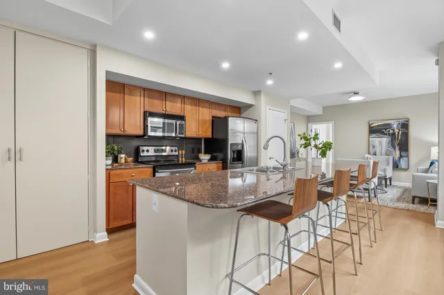 a kitchen with stainless steel appliances granite countertop a refrigerator a stove a sink a dining table and chairs with wooden floor