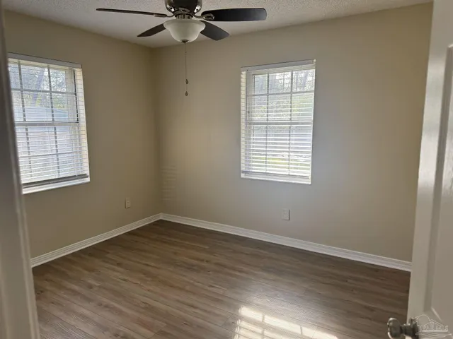 an empty room with wooden floor windows and fan