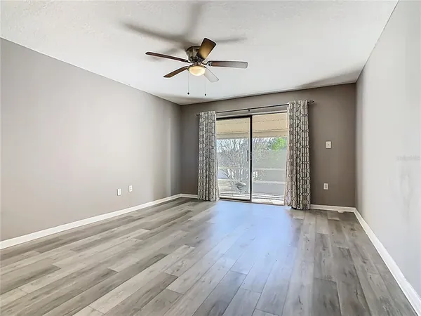 an empty room with wooden floor fan and windows