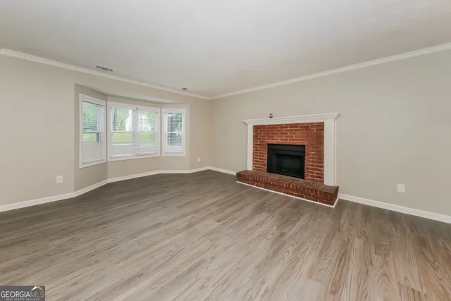 an empty room with wooden floor fireplace and windows