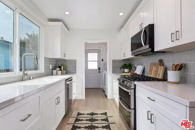 a kitchen with stainless steel appliances granite countertop a sink stove oven and white cabinets with wooden floor