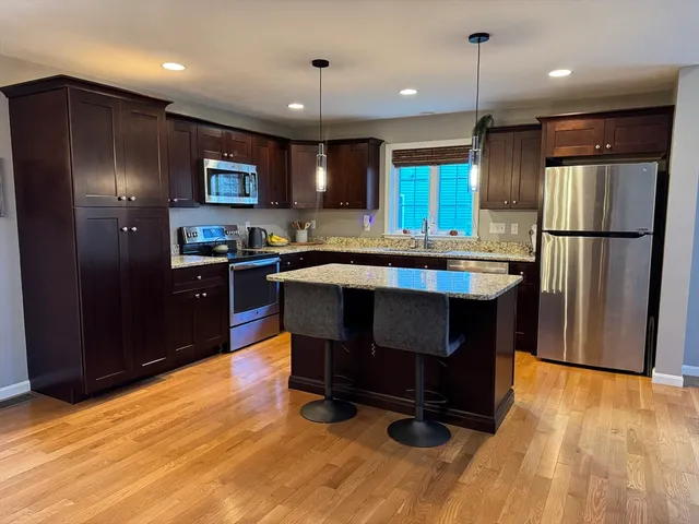 a kitchen with stainless steel appliances granite countertop a refrigerator a sink dishwasher a stove and a refrigerator with wooden floor