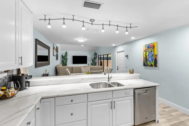 a kitchen with a sink dishwasher and white cabinets with wooden floor