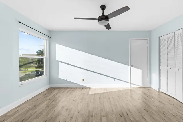an empty room with wooden floor fan and windows