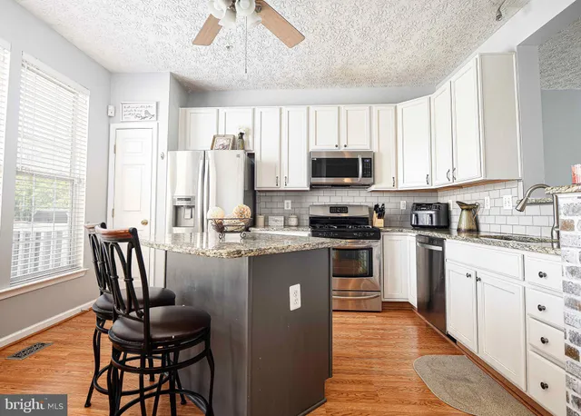 a kitchen with stainless steel appliances granite countertop a stove top oven a sink dishwasher a dining table and chairs with wooden floor