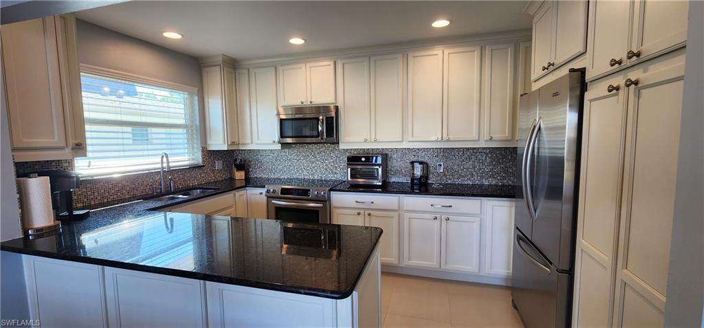 75 Georgetown Boulevard, Unit 75 Naples, FL 34112 - Photo 8 of 28 Kitchen with backsplash, white cabinets, countertops. appliances with stainless steel finishes