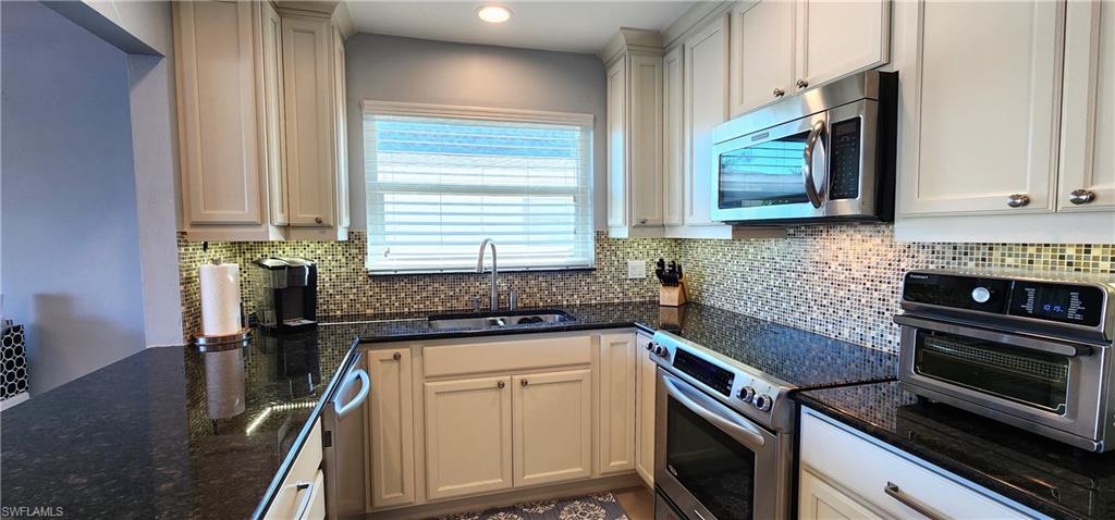 75 Georgetown Boulevard, Unit 75 Naples, FL 34112 - Photo 10 of 28 Kitchen with appliances with stainless steel finishes, tasteful backsplash, sink, dark stone countertops, and white cabinetry