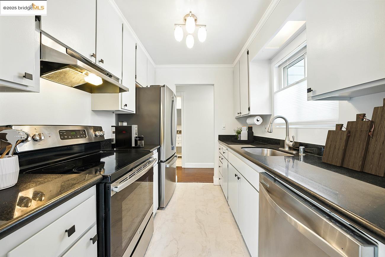 567 Oakland Avenue, Unit 101 Oakland, CA 94611 - Photo 5 of 50 Kitchen with appliances with stainless steel finishes, under cabinet range hood, white cabinets, ornamental molding, and light marble finish floors