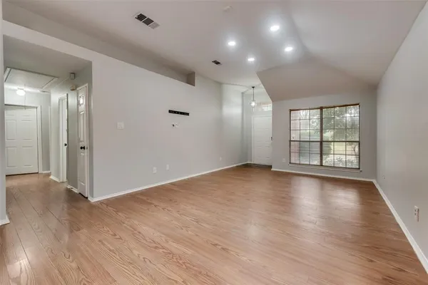 a view of an empty room with wooden floor and a window