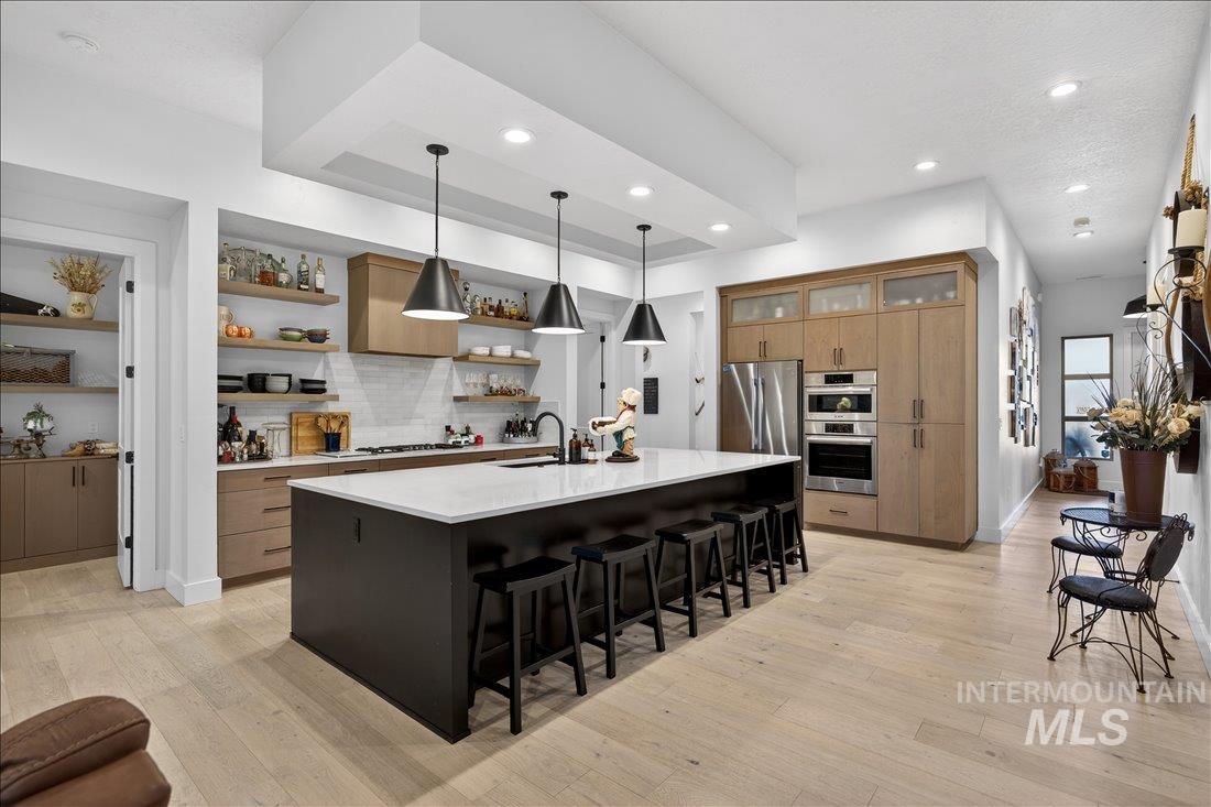 4718 East Goldstone Drive Meridian, ID 83642 - Photo 12 of 50 Dual tone kitchen with a center island with sink, light wood finished floors, hanging light fixtures, a kitchen breakfast bar, and light stone countertops